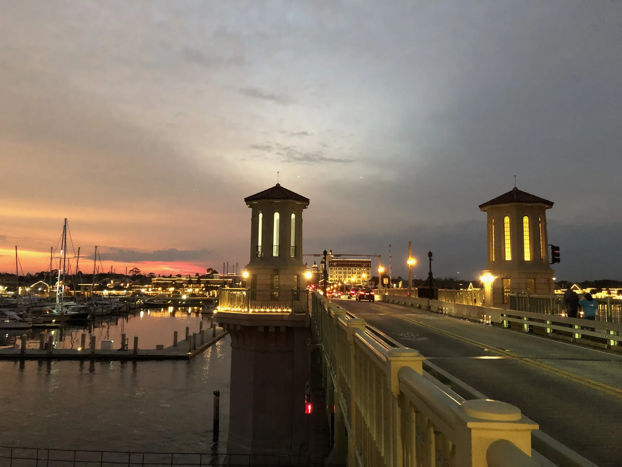 The Bridge of Lions lit up at dusk, with boats in the marina and a pink sky behind it.