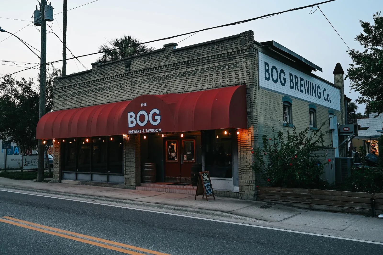 The Bog Brewing Company storefront at dusk: a red awning, string lights and a chalkboard sign on West King Street.